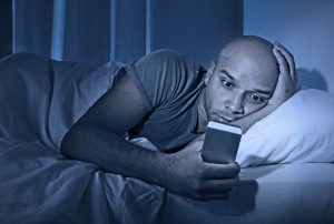 Man on phone at night, which is keeping him awake